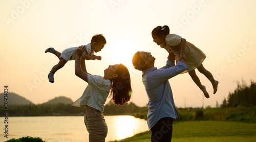 Happy father and mother holding children playing together in park photo