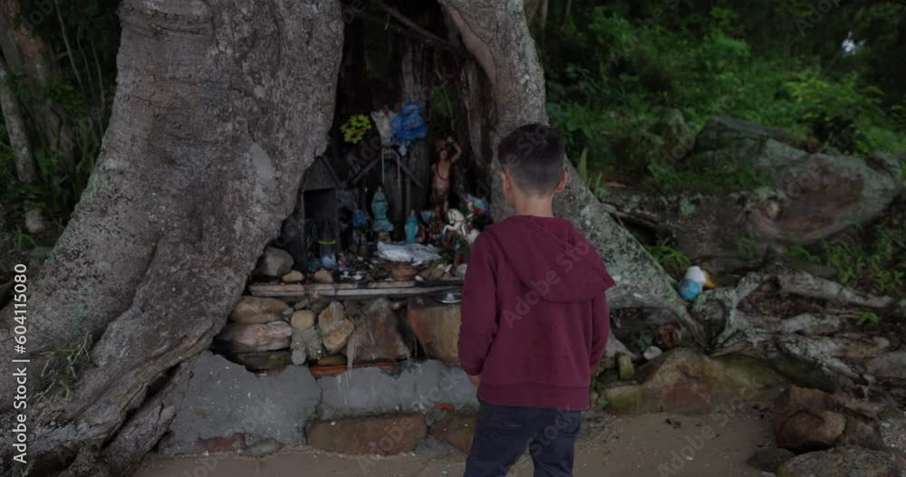 Young boy explores beach shrine set up inside tree on tropical island Young boy explores beach shrine set up inside tree on tropical island