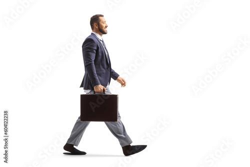 Full length profile shot of a man wearing a suit and bottom pajamas and walking with a briefcase