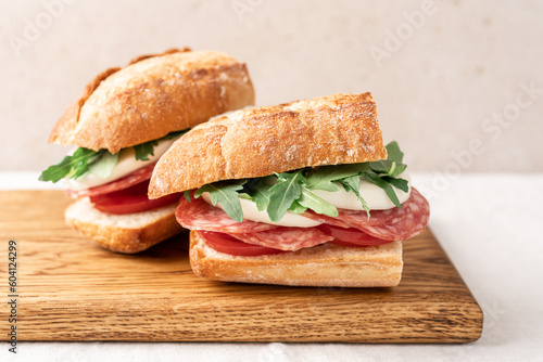Italian sandwich with baguette, mozzarella, salami and arugula. Picnic sandwich on wooden board close up view