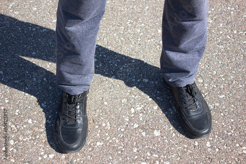 Men's feet in boots on the pavement. A man stands in black shoes on the road, close-up of his legs.