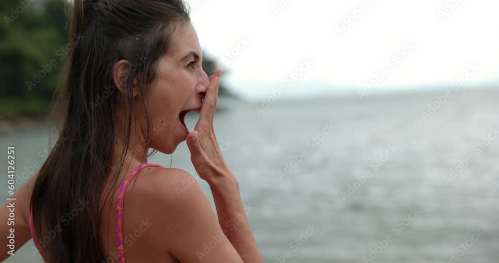 Woman stands on beach overlooking ocean in morning yawns - side profile Woman stands on beach overlooking ocean in morning yawns - side profile