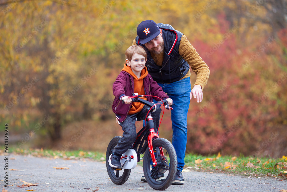 Obraz premium Father teaching his little son to ride bicycle in park. Bearded man helping child to learn bike. Family values, child support, fathers day concept. Selective focus.