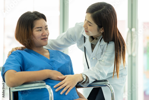 woman obstetrician doctor look holding hand to consoling encourage woman pregnant patient on wheelchair in hospital. woman doctor talk diagnosis treatment for mother pregnancy