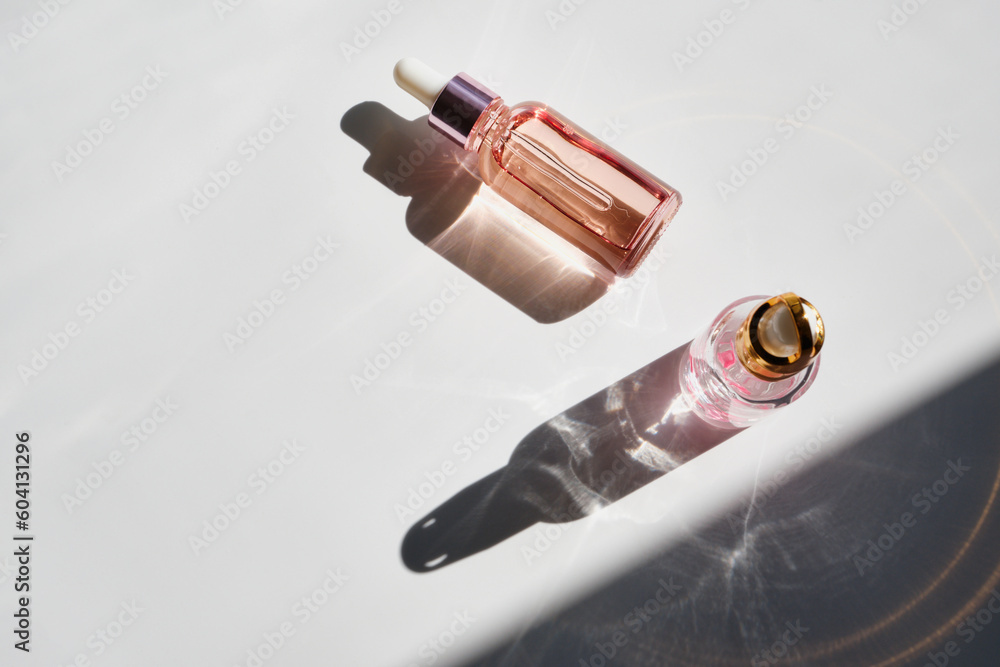 Cosmetic product bottles with rose petals and hard shadow. Skincare beauty product concept - obrazy, fototapety, plakaty 