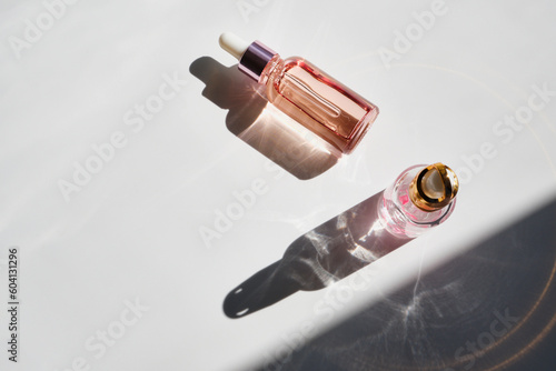 Cosmetic product bottles with rose petals and hard shadow. Skincare beauty product concept