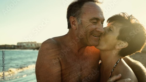 Happy senior couple having a romantic moment on the beach at sunset during summer vacations - Elderly people relationship concept 