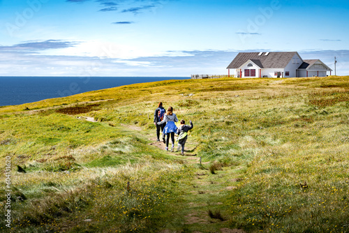 Family on vacation running across a grassy field overlooking high cliffs and the Atlantic Ocean at Cape St. Mary's Ecological Reserve Newfoundland Canada.