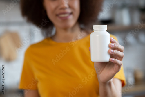 Happy young smiling African American woman holding bottle of dietary supplements or vitamins in hands, close up. selective focus. Healthy lifestyle concept