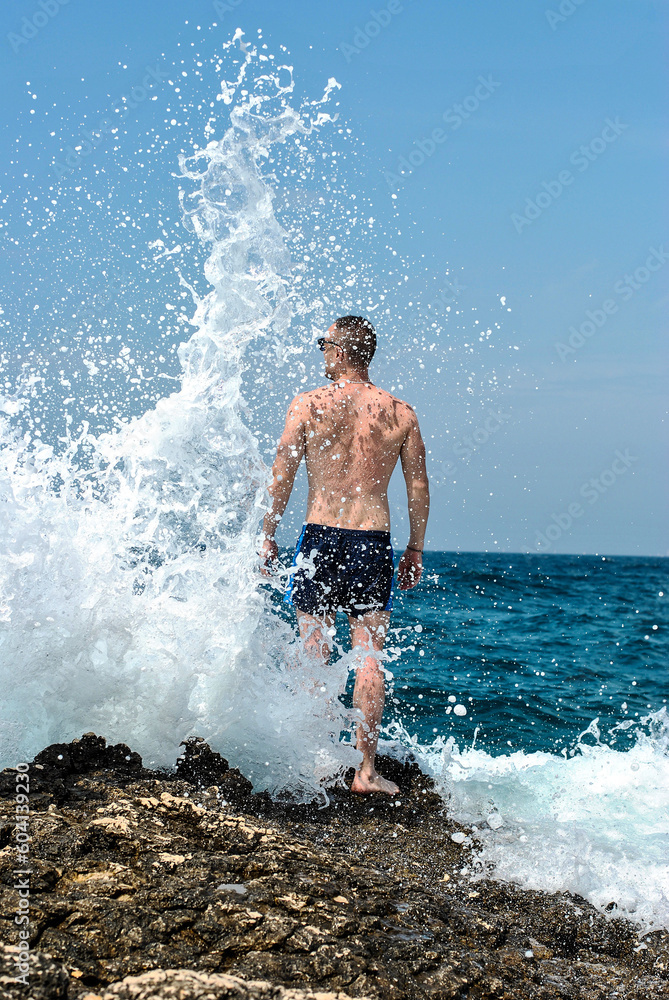 Bathing With Rocks Man standing on a rock as a wave crashes over the rocks creating a very ...