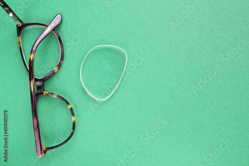 Old broken eyeglasses with damaged lens on green background. Poor eyesight. Reuse and repair concept. Idea of health. Failure optic eyewear. Breakage of vision correction glasses. Close up, flat lay