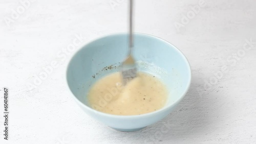 Yoghurt salad dressing is whipped with a fork in a light blue bowl on a light gray tabletop photo