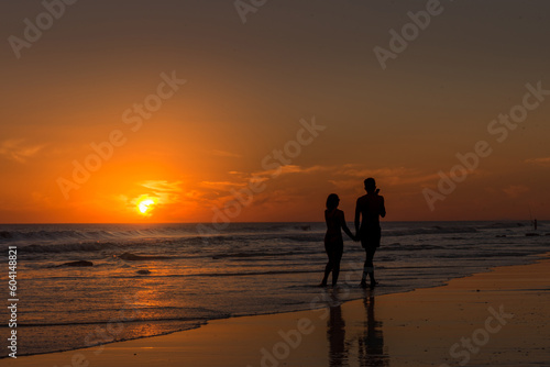Couple holding hands while walking along the seashore on the beach at sunset.