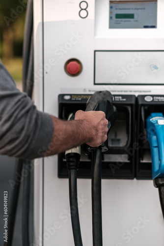 Person taking  a CCS charging cable at a fast charging station to charge an electric car.