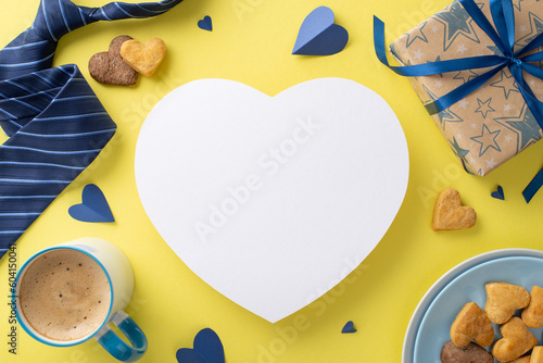 Homemade Father's Day breakfast: Top view plate of biscuits, cup of coffee, hearts, accessories, necktie, and giftbox on bright yellow background with empty heart for advertising or message