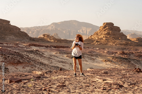 Young red haired girl with camera in hands in the rocky desert Sinai Egypt
