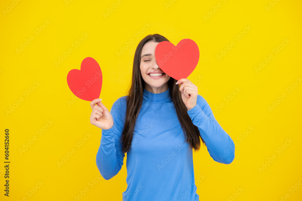 Valentines Day. Beautiful young woman with heart in her hands. Attractive woman with paper heart over yellow background. Valentines Day. Beautiful young woman with heart in her hands. Attractive woman with paper heart over yellow background.