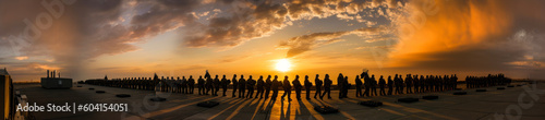 Stunning sunset image with silhouetted soldiers carrying fallen comrade on a stretcher, evoking emotions of heroism, loss & camaraderie; ideal for military-themed projects. Generative AI