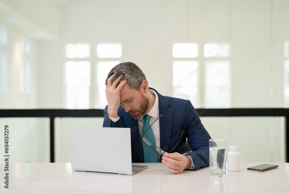 Headache, tiredness and stress. Business man in suit uses a laptop, is tired got headache migraine. Headache pain concept. Painful men are stressed at work in office. Stressful and headache. Headache, tiredness and stress. Business man in suit uses a laptop, is tired got headache migraine. Headache pain concept. Painful men are stressed at work in office. Stressful and headache.