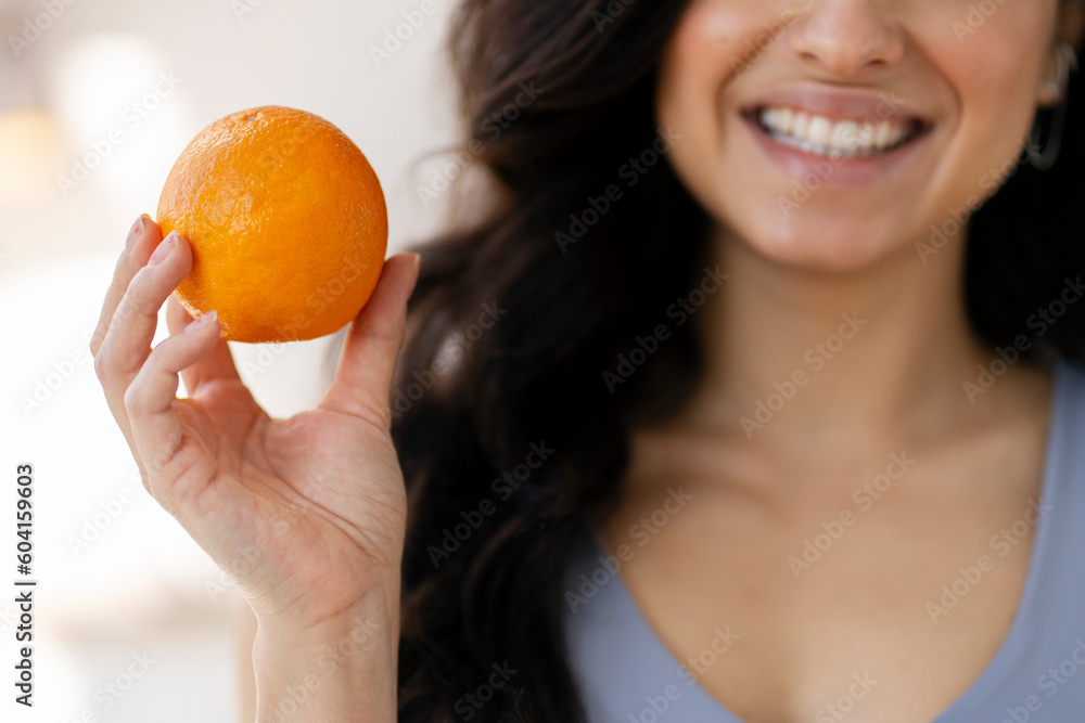Cropped portrait of brunette cheerful woman holding orange, standing in kitchen Cropped portrait of brunette cheerful woman holding orange, standing in kitchen