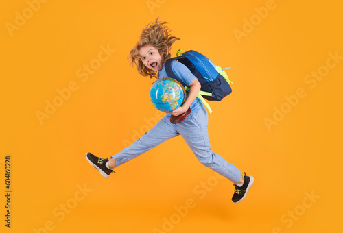 Shool kid jump with school bag and globe. School child in school uniform with bagpack and globe jump. School children jumping on studio isolated yellow background.