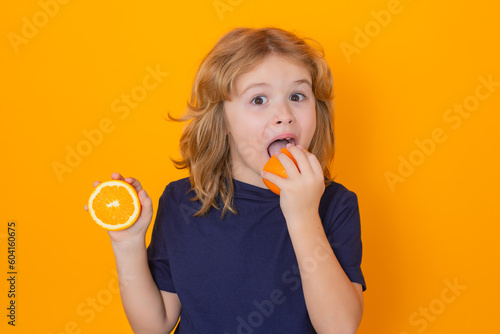 Citrus. Kid eat orange in studio. Studio portrait of cute child lick orange isolated on yellow background.