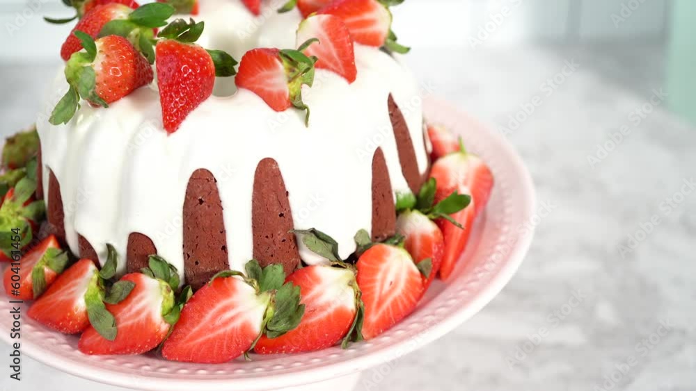 Red velvet bundt cake with cream cheese frosting garnished with fresh strawberries on a pink cake stand for Valentines Day. Red velvet bundt cake with cream cheese frosting garnished with fresh strawberries on a pink cake stand for Valentines Day.