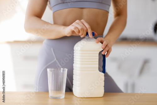 Fit young woman hands opening bottle with fresh oat milk, standing in kitchen