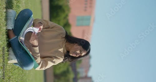 Young teenage Latina college student studying for an exam in an outdoor park with books, vertical shot