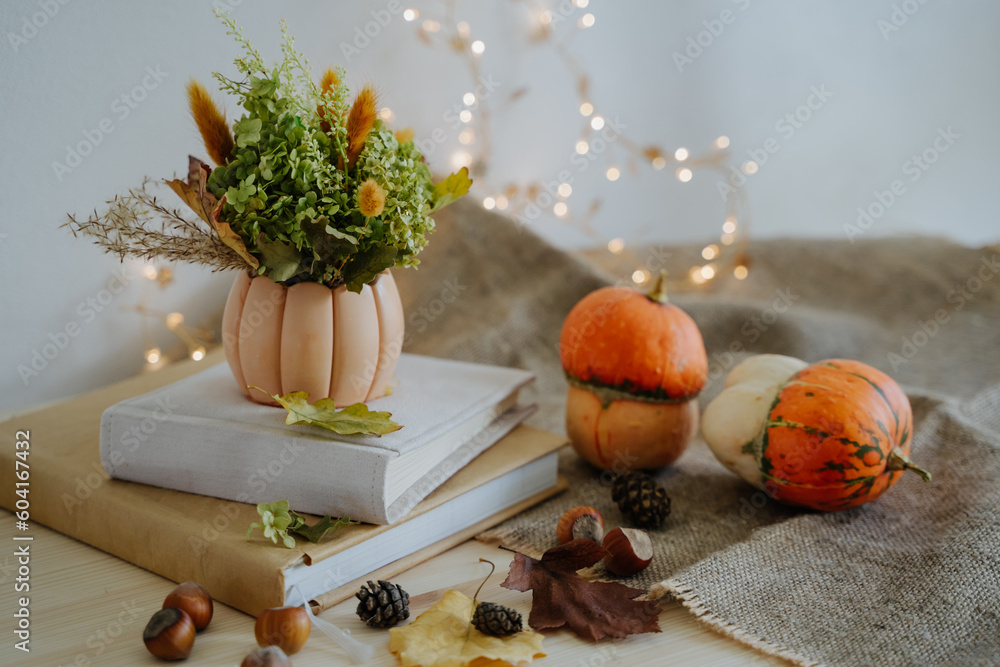 Autumn composition of books, pumpkins, nuts, autumn leaves, a bouquet of dried flowers, cones. Pumpkin and nuts. Garland with warm light. Bokeh. Thanksgiving Day. Festive composition. Autumn composition of books, pumpkins, nuts, autumn leaves, a bouquet of dried flowers, cones. Pumpkin and nuts. Garland with warm light. Bokeh. Thanksgiving Day. Festive composition.