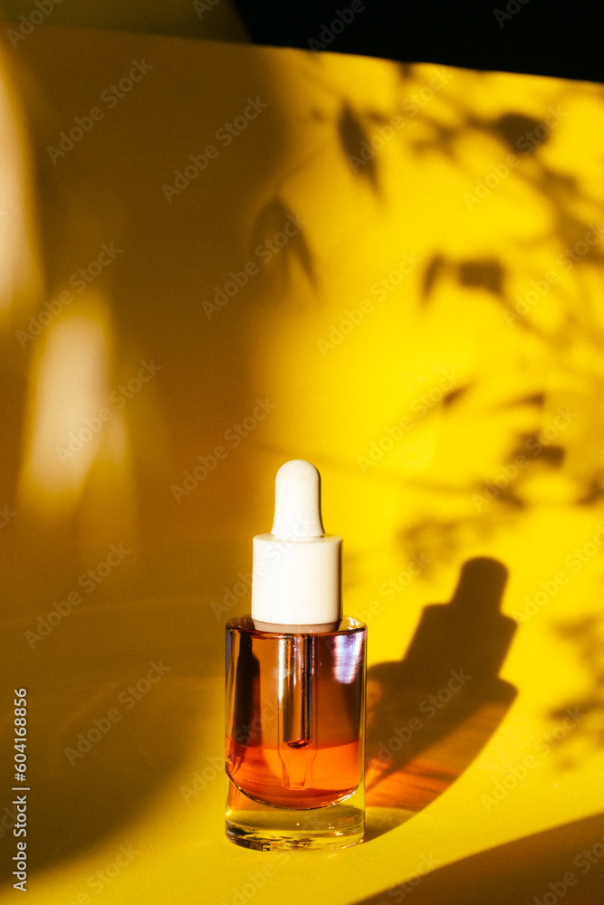 Glass cosmetic jar with serum for face and body skin care on yellow background. Grooming cosmetics for women. Female beauty tool and cosmetic. Face serum on natural backdrop with plants shadows. Glass cosmetic jar with serum for face and body skin care on yellow background. Grooming cosmetics for women. Female beauty tool and cosmetic. Face serum on natural backdrop with plants shadows.