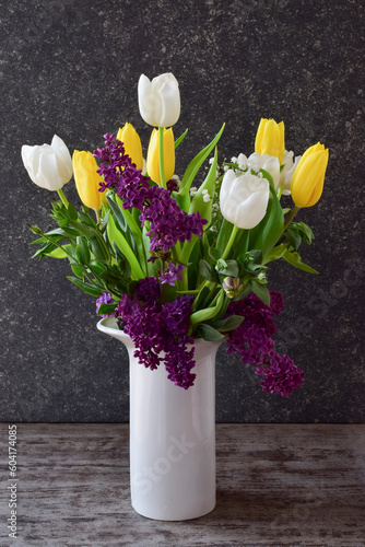 A beautiful bouquet of tulips and lilacs in a white vase, side view