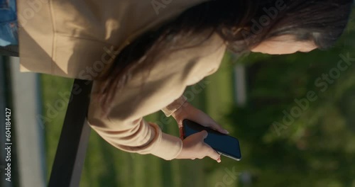 Young teenage Latina college student using social networks with her smartphone in a park, vertical shot