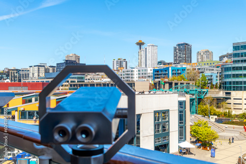 A tower viewing telescope binoculars is blurred in the foreground as the skyline of Seattle, Washington USA is in focus behind, including the Seattle Space Needle.
