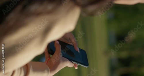 Young teenage Latina college student using social networks with her smartphone in a park, vertical shot