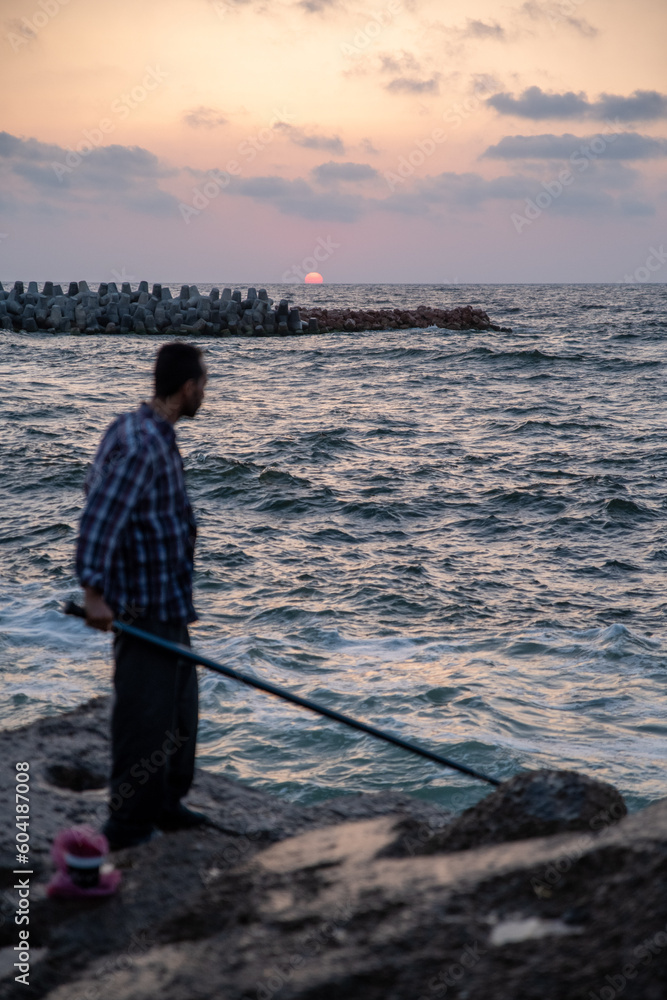 A man fishing by the sea with red orange beautiful sunset