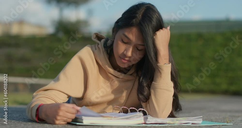 Young teenage Latina college student studying for an exam in an outdoor park with books