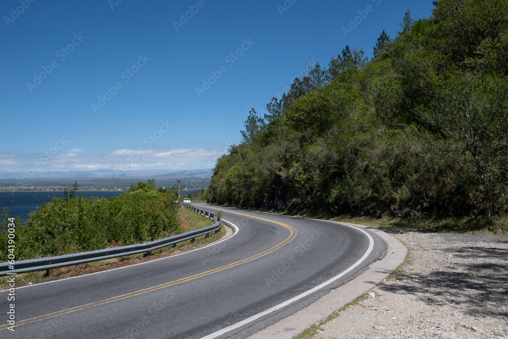 
Route in the mountain between trees with guardrail. No people. Daytime, clear sky.