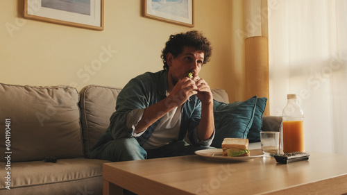 Guy dressed in denim shirt has lunch, sits in the living room and emotionally watches sports game on TV