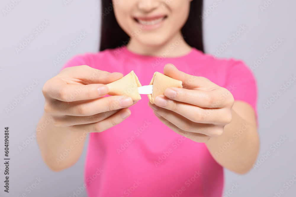 Young woman holding tasty fortune cookie with prediction on grey background, closeup Young woman holding tasty fortune cookie with prediction on grey background, closeup