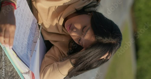 Young teenage Latina college student studying for an exam in an outdoor park with books, vertical shot