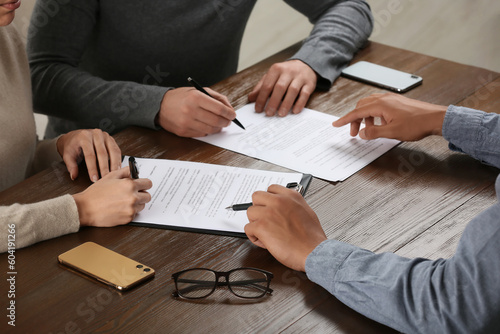 Notary helping couple with paperwork at wooden table, closeup