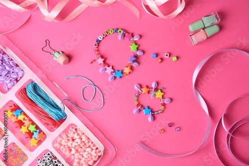 Handmade jewelry kit for kids. Colorful beads, ribbons and bracelets on bright pink background, flat lay