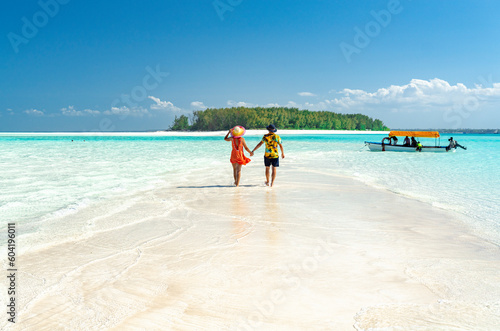 Man and woman in love holding hands walking on empty sandy shore surrounded by the Indian Ocean, Zanzibar, Tanzania photo