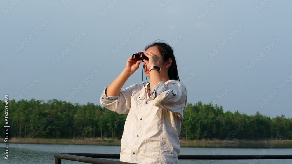 Young female explorer with binoculars exploring nature or watching birds outdoors. Young woman looking through binoculars at birds on the reservoir. Birdwatching Young female explorer with binoculars exploring nature or watching birds outdoors. Young woman looking through binoculars at birds on the reservoir. Birdwatching
