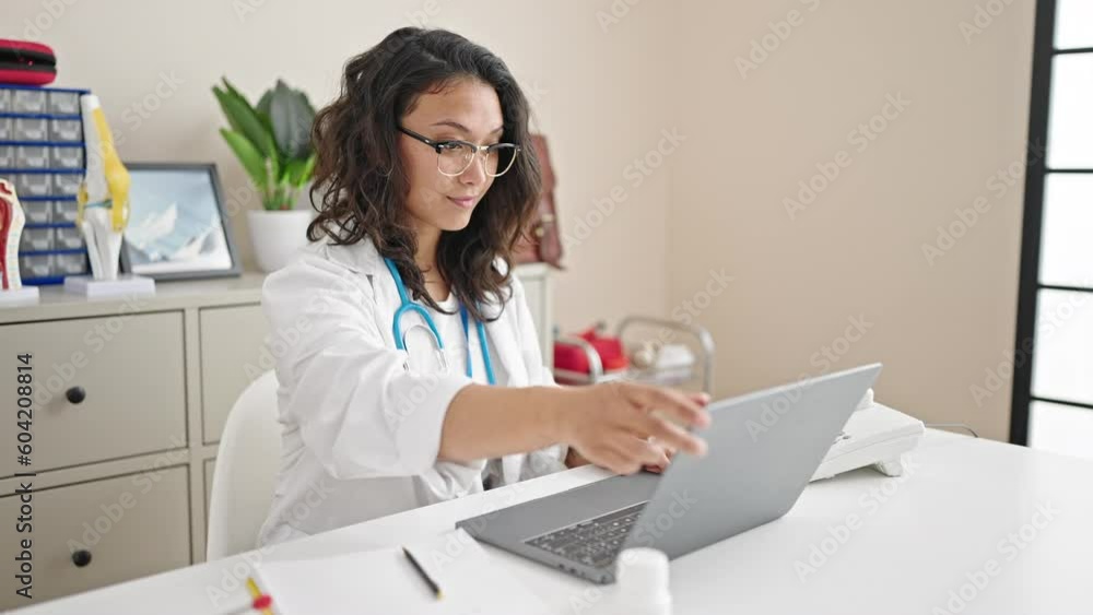 Young beautiful hispanic woman doctor opening laptop working at clinic Young beautiful hispanic woman doctor opening laptop working at clinic