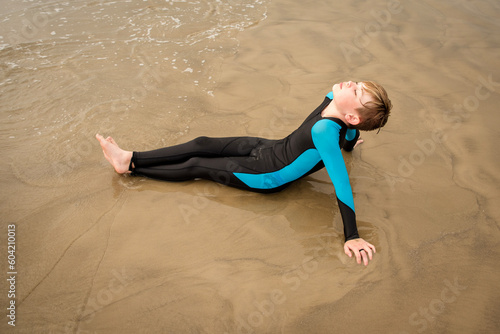 Φωτογραφία Preteen boy in wetsuit sitting back relaxing on a wet sandy beach