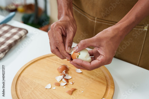 Close-up of a man's hand peeling a hard-boiled egg to prepare the salad and sandwiches for breakfast. Before going to work, gently peel off the shell of the egg until it's unappetizing.