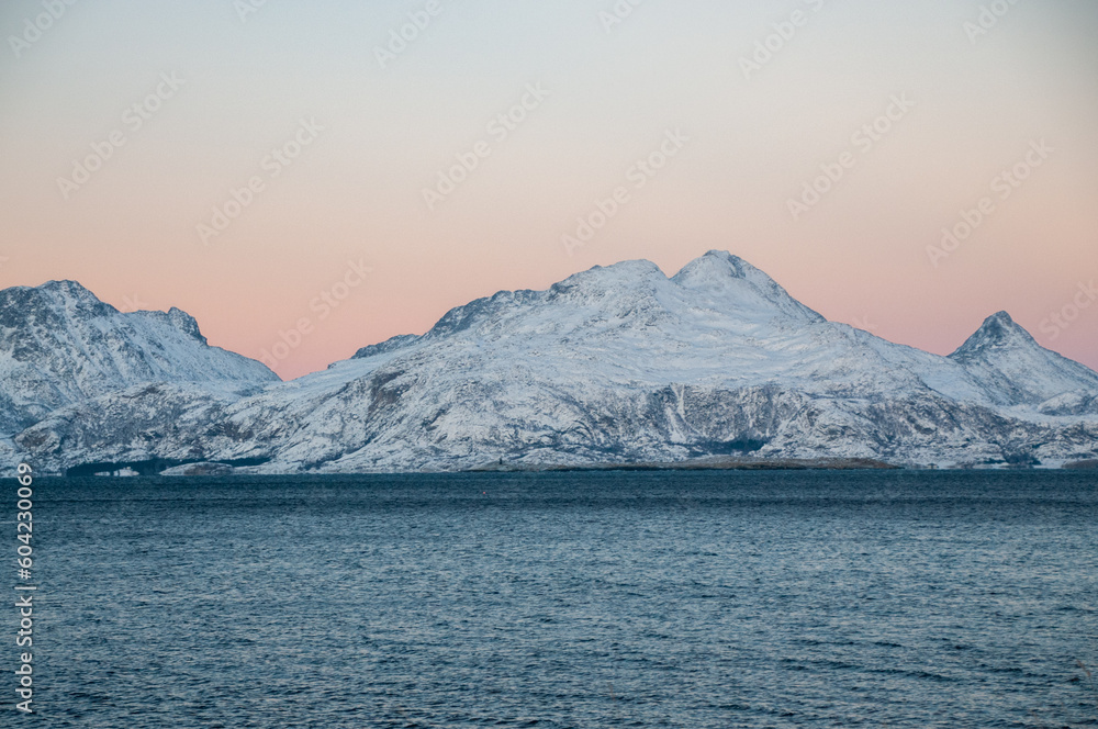 Landscape shot highlighting the rugged mountains and snow-covered beaches of arctic norway during a brief golden hour during the long winters.