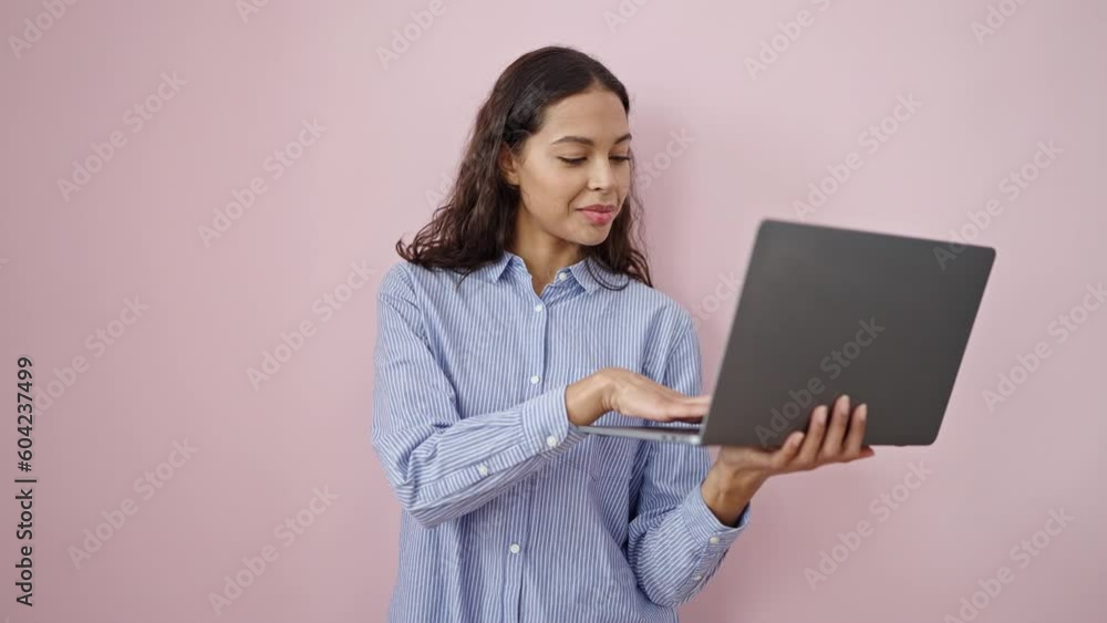 Young beautiful hispanic woman smiling holding laptop over isolated pink background Young beautiful hispanic woman smiling holding laptop over isolated pink background